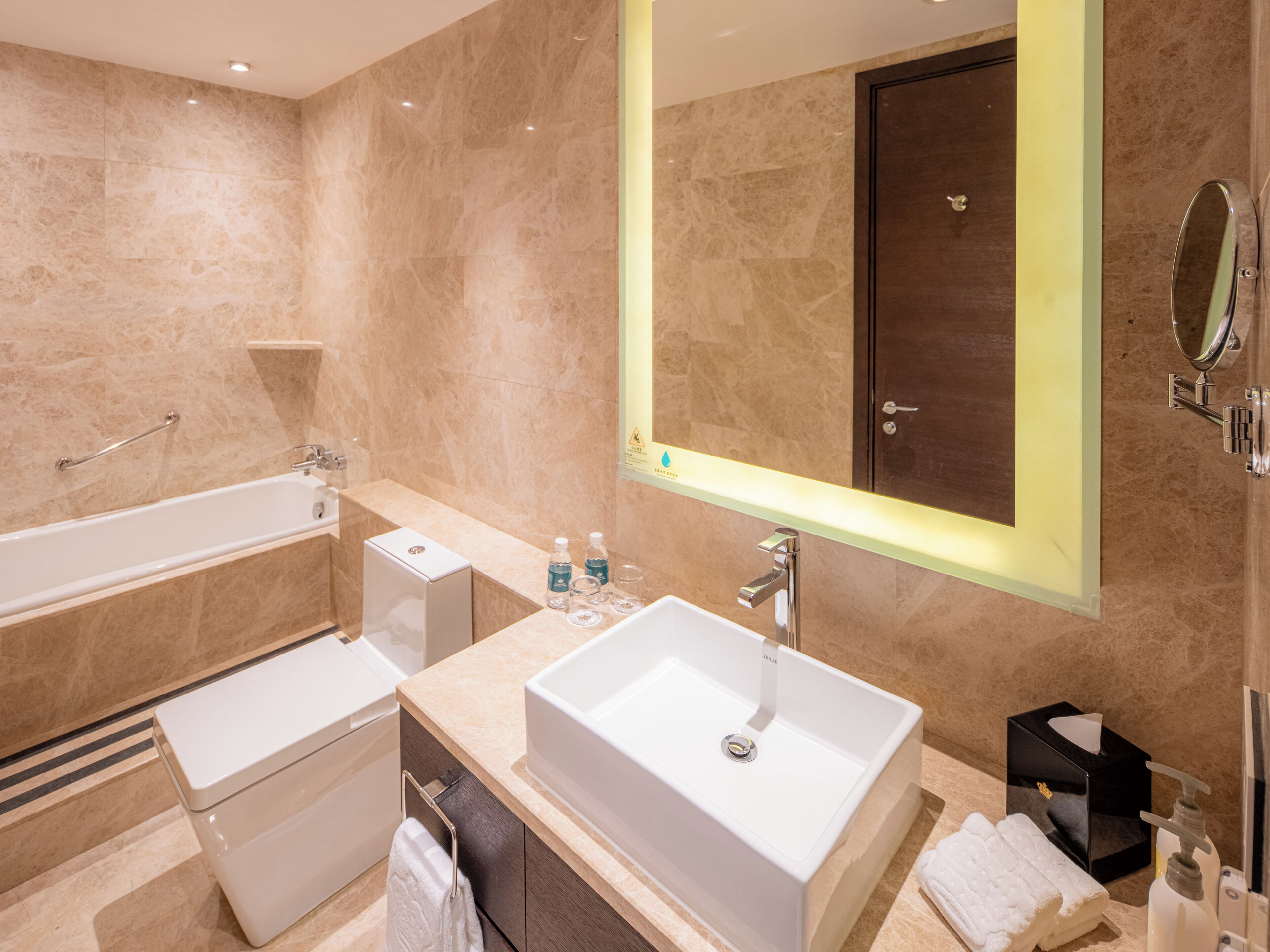 A modern bathroom with a large mirror, a bathtub, a sink, and a toilet.