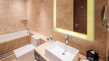 A modern bathroom with a large mirror, a bathtub, a sink, and a toilet.
