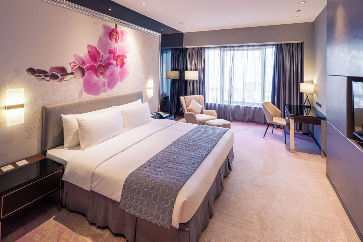A hotel room with a large bed, a desk, a chair, and a TV.