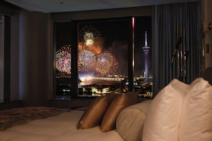 A hotel room with a large window overlooking a cityscape and fireworks display.