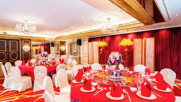 Un salón de banquetes con mesas redondas dispuestas para un evento formal, con manteles rojos y sillas blancas.