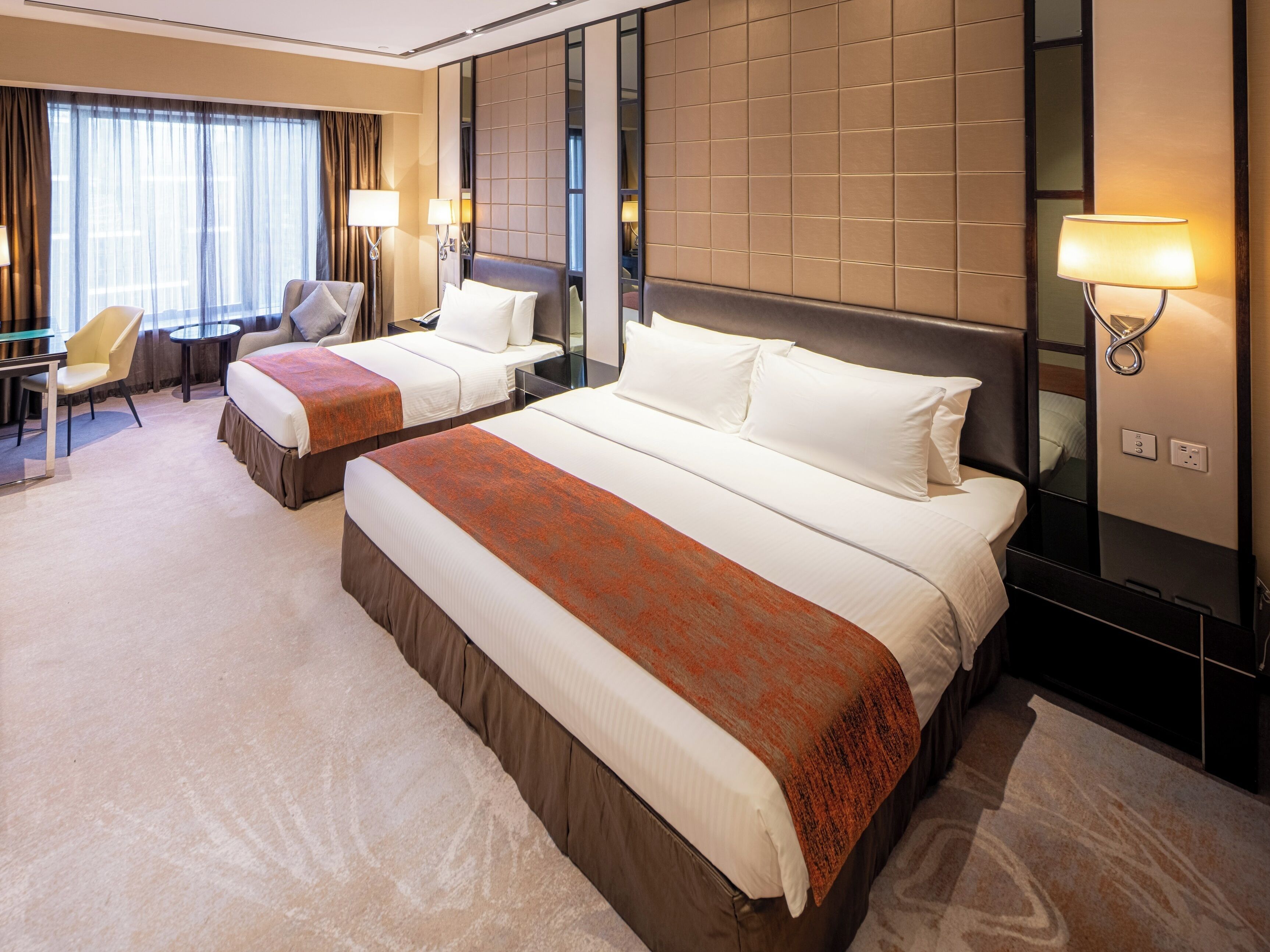 A hotel room with two beds, a desk, a chair, and a large mirror.