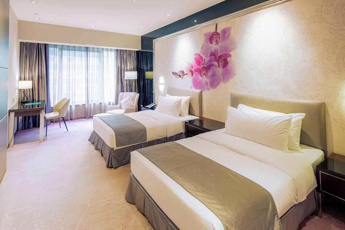 A hotel room with two beds, a desk, a chair, and a large floral wall decoration.