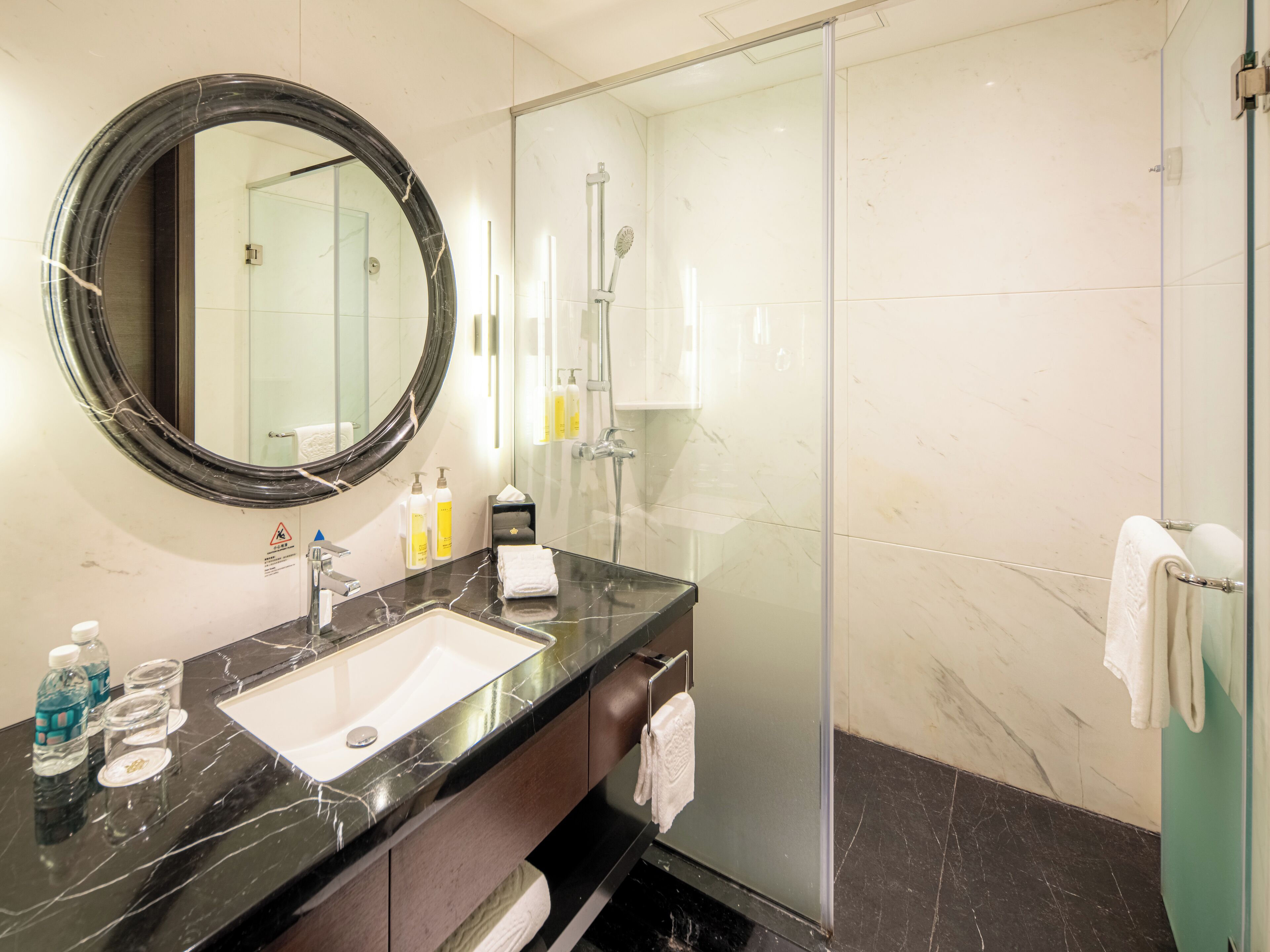 A modern bathroom with a black marble sink, a large mirror, and a glass shower enclosure.