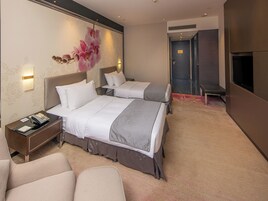 Habitación de hotel con dos camas, un escritorio, una silla y una obra de arte floral grande en la pared.