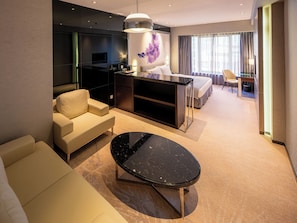 A modern hotel room with a sofa, a black marble coffee table, a bed, a desk, and a large window with curtains.