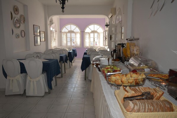 Spiseområde med borde dækket til et måltid, en buffet med forskellige retter og udsigt udad gennem buede vinduer.