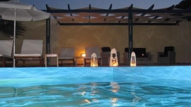 A swimming pool with clear water, lounge chairs, and umbrellas. - Melina Hotel (Santorini)