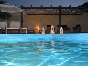En swimmingpool med klart vand, liggestole og parasoller.