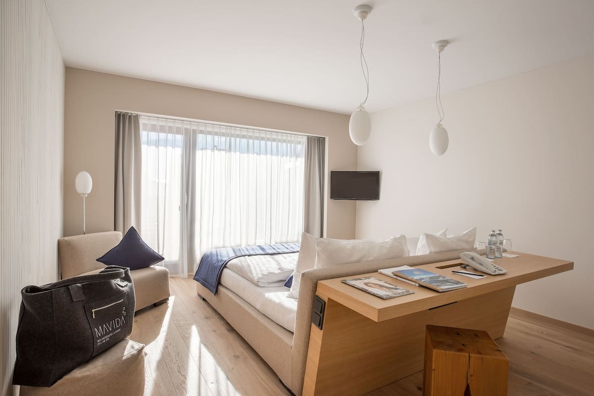 Ett hotellrum med en säng, ett skrivbord, en stol, en tv och en väska.
