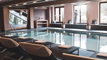 A modern indoor swimming pool with lounge chairs and a view of the outdoors.