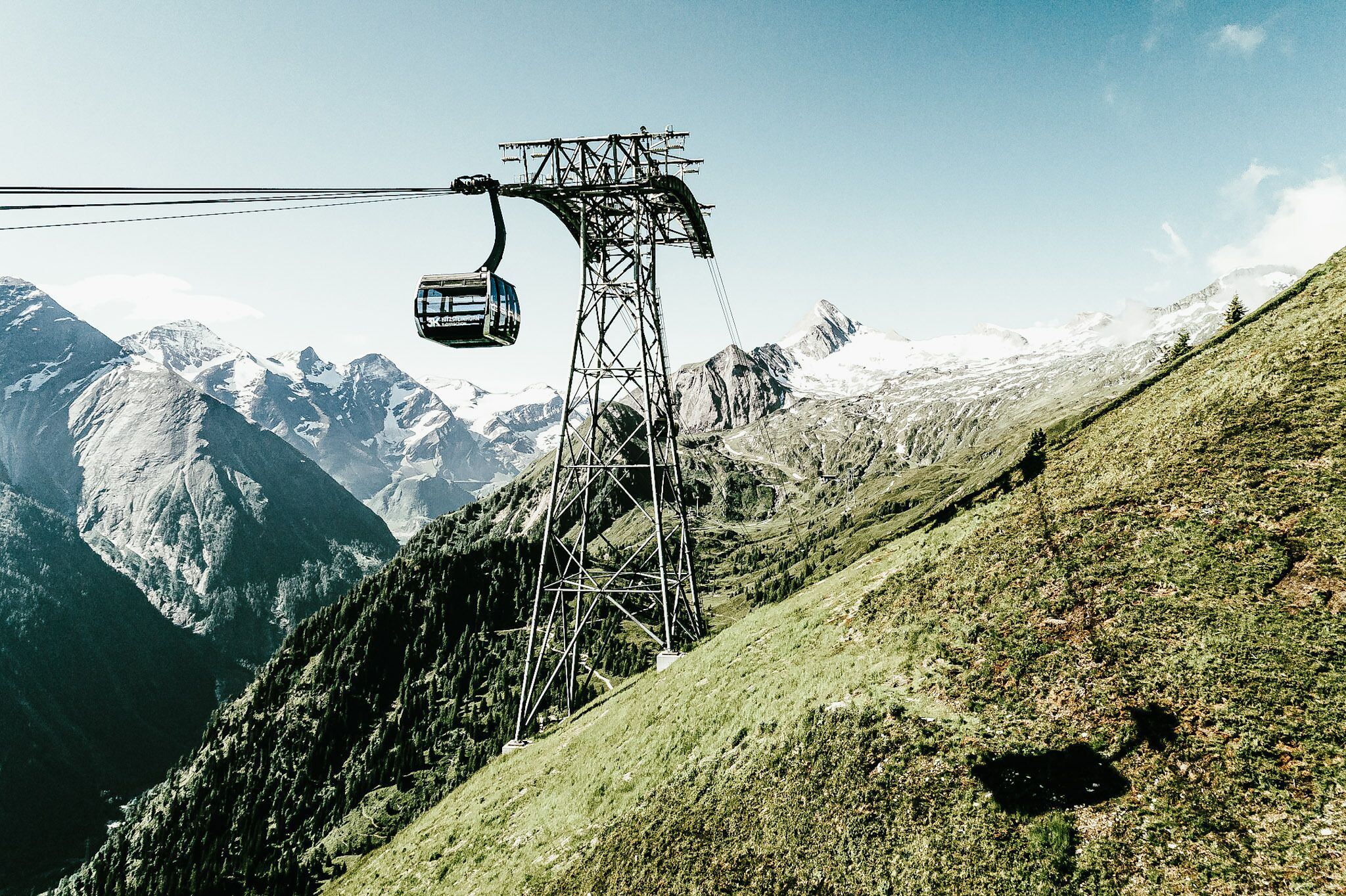 Un sistema de teleférico en una zona montañosa con picos nevados al fondo.