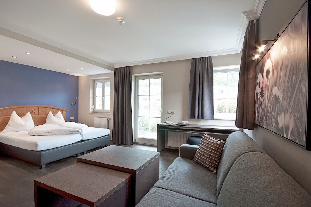 Ett hotellrum med en säng, en soffa, ett skrivbord och ett stort fönster.