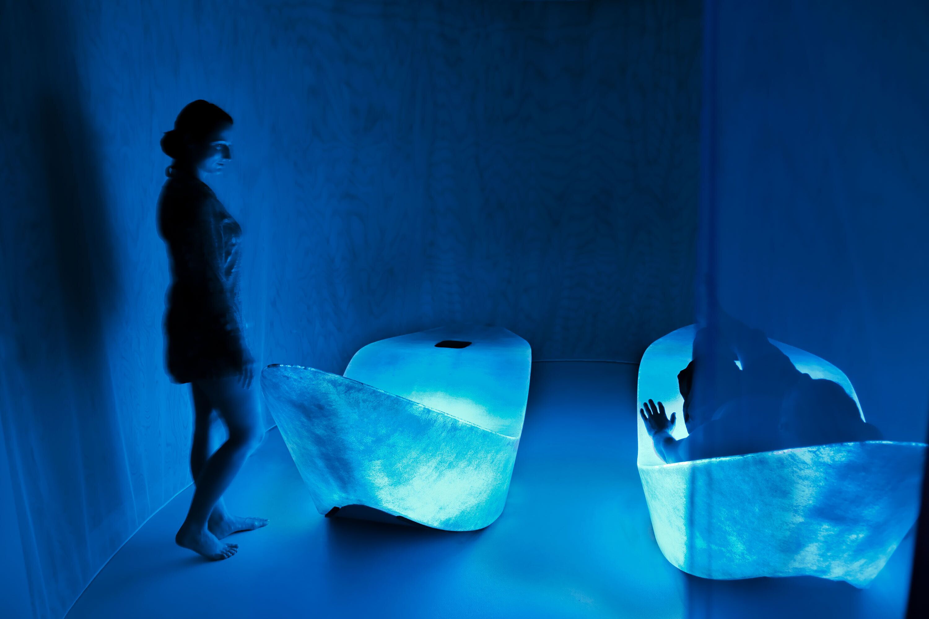 A person walking through a room with two glowing, translucent chairs.