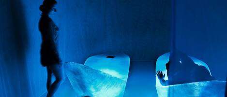 A person walking through a room with two glowing, translucent chairs.