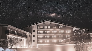 A multi-story hotel with a pool area, featuring a large building with balconies and a clear night sky.