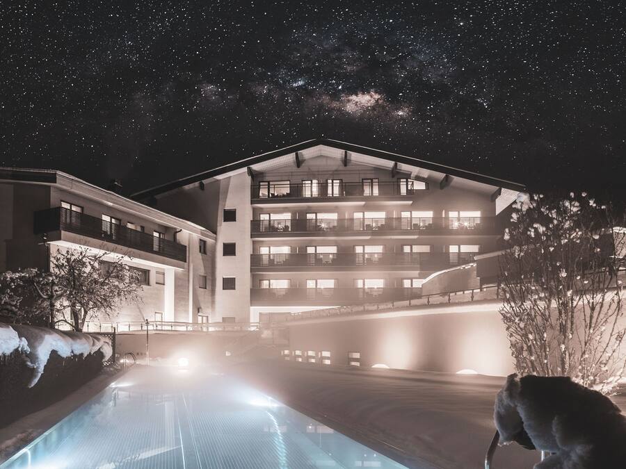 Un hotel de varios pisos con zona de piscina, destacando un edificio con balcones y un cielo nocturno despejado.