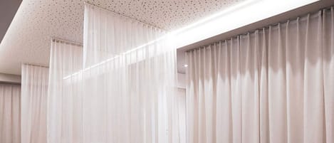 A modern hotel room with a large bed, a mirror, and sheer curtains.