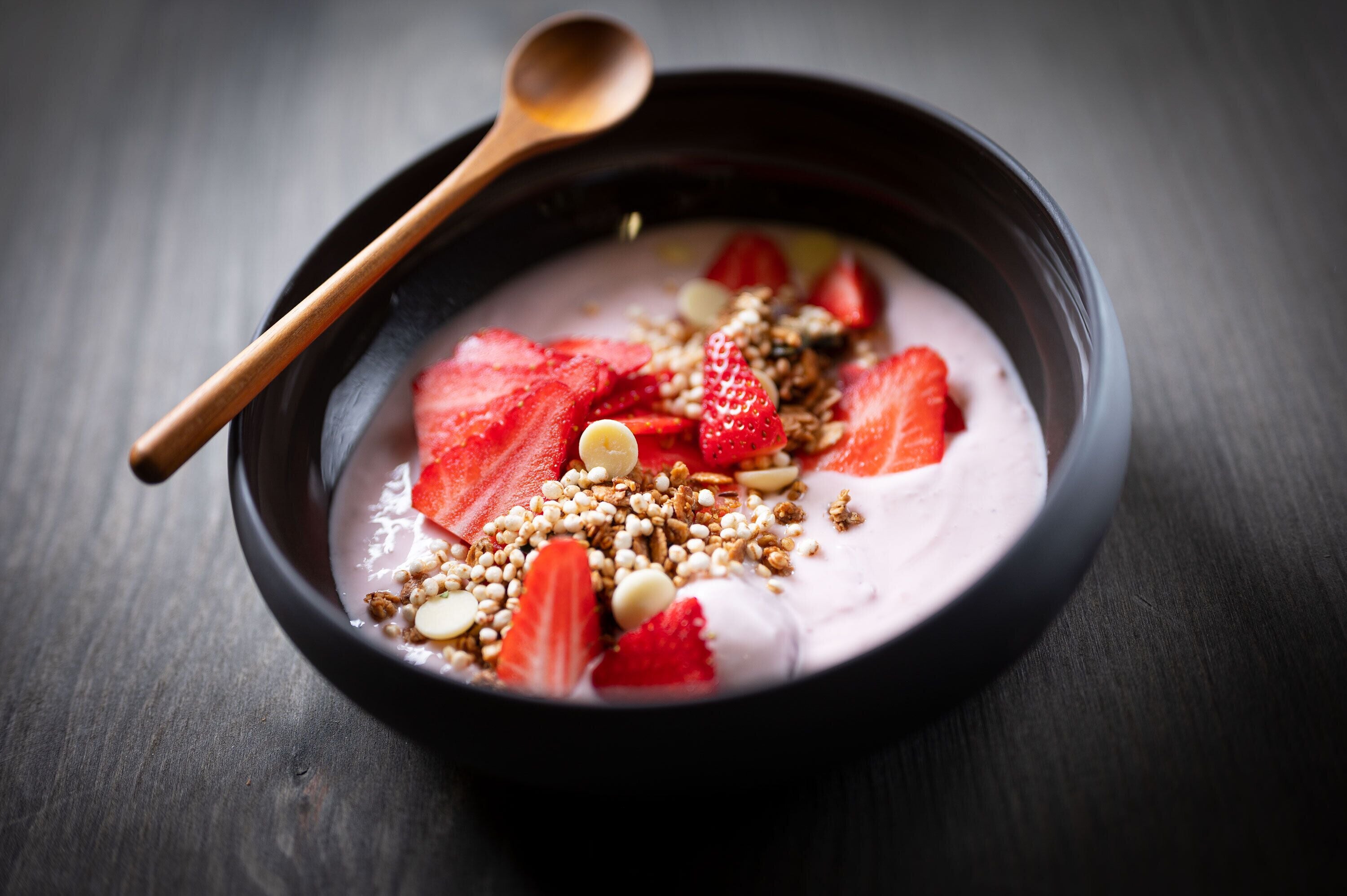 Un tazón de yogur con fresas y granola sobre una superficie oscura.