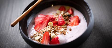 Un tazón de yogur con fresas y granola sobre una superficie oscura.