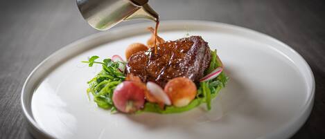 Un chef vertiendo salsa sobre un plato con carne y verduras.