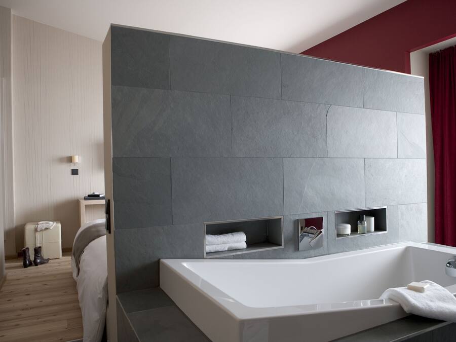 A modern bathroom with a large bathtub, built-in shelves, and a wooden floor.