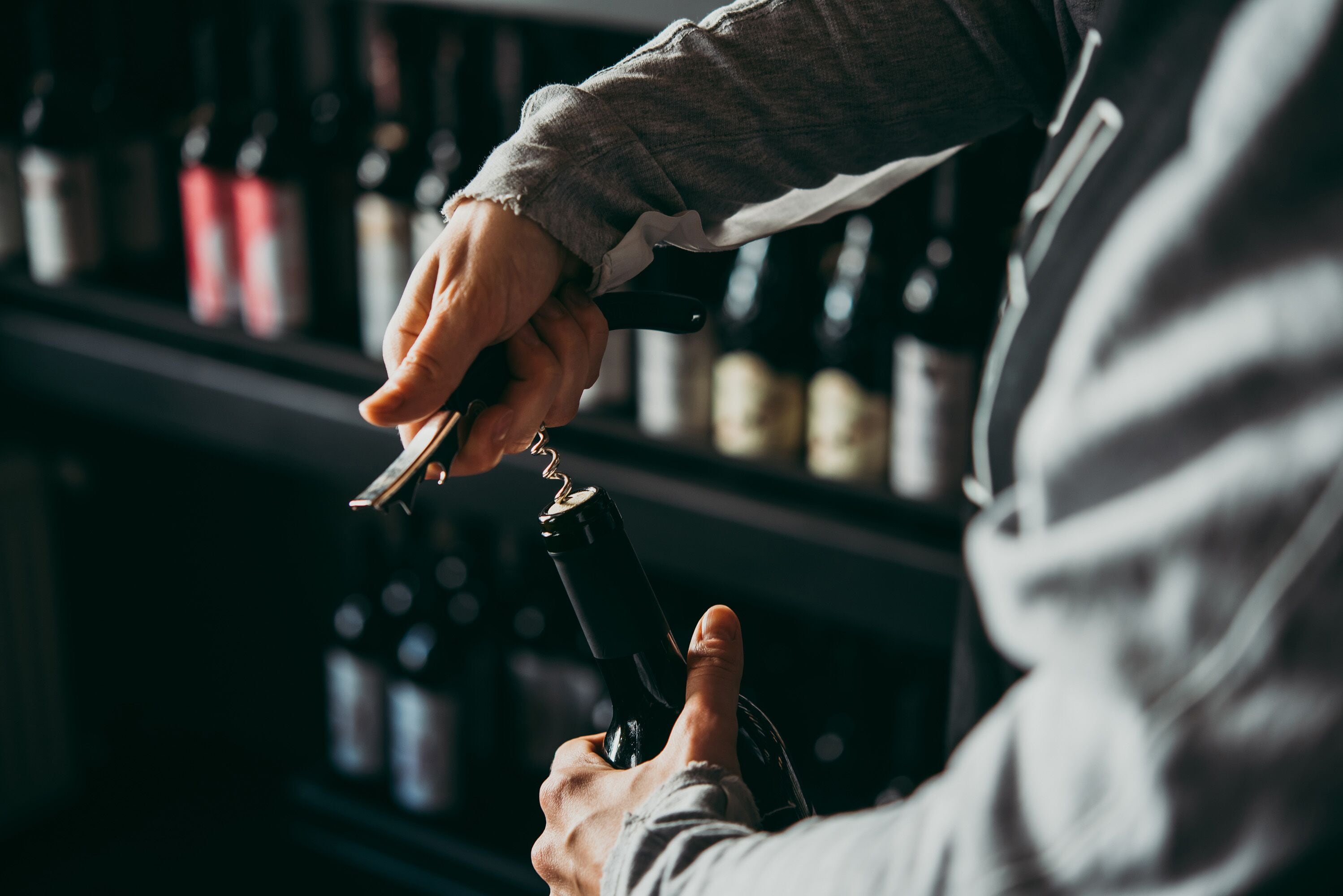 A person opening a bottle of wine with a corkscrew.