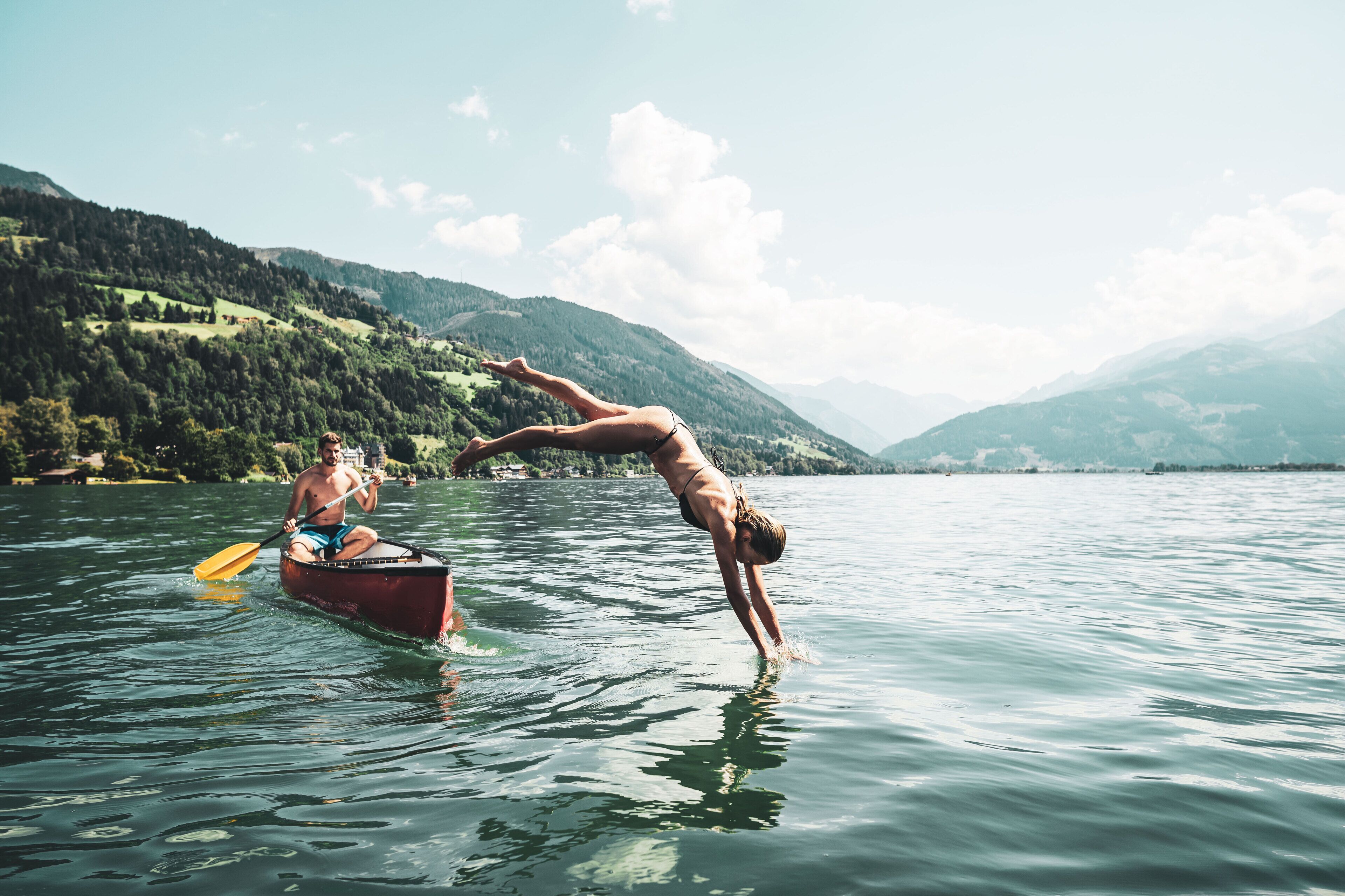 A person performing a handstand in a boat on a lake with mountains in the background.