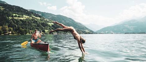 A person performing a handstand in a boat on a lake with mountains in the background.