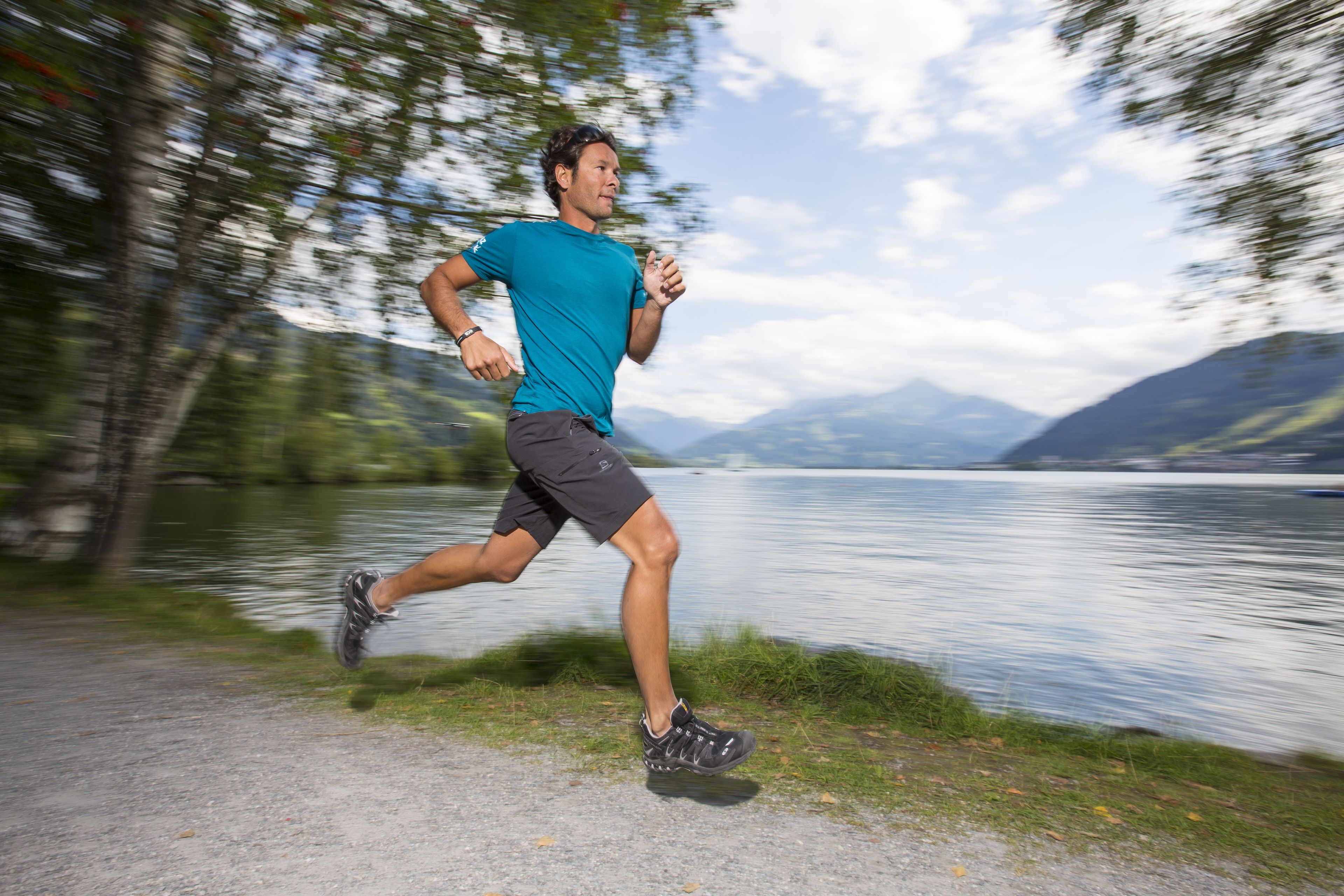 A person running along a path beside a lake with mountains in the background.