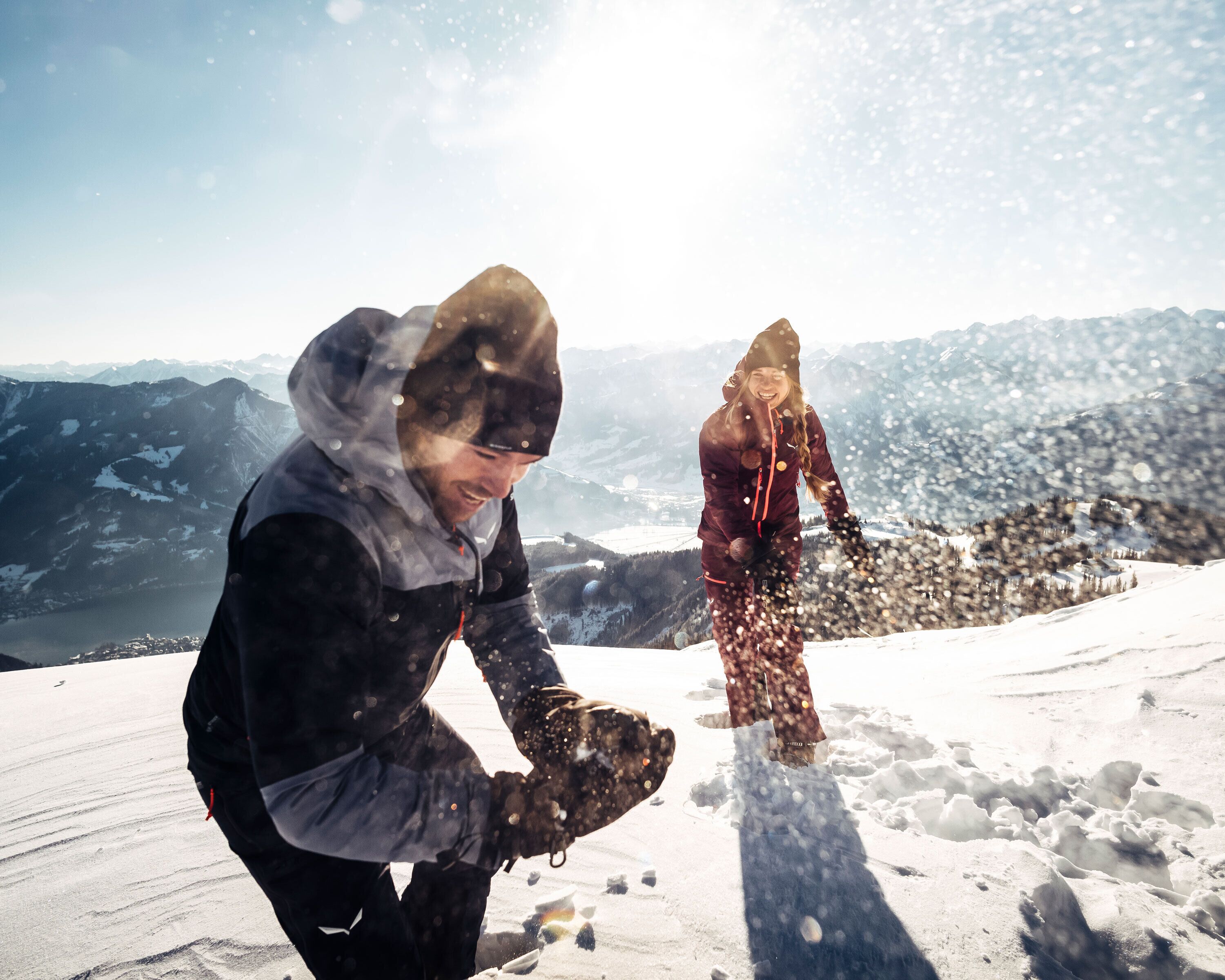 Two people on a snowy mountain with a clear view of distant mountains and a valley.