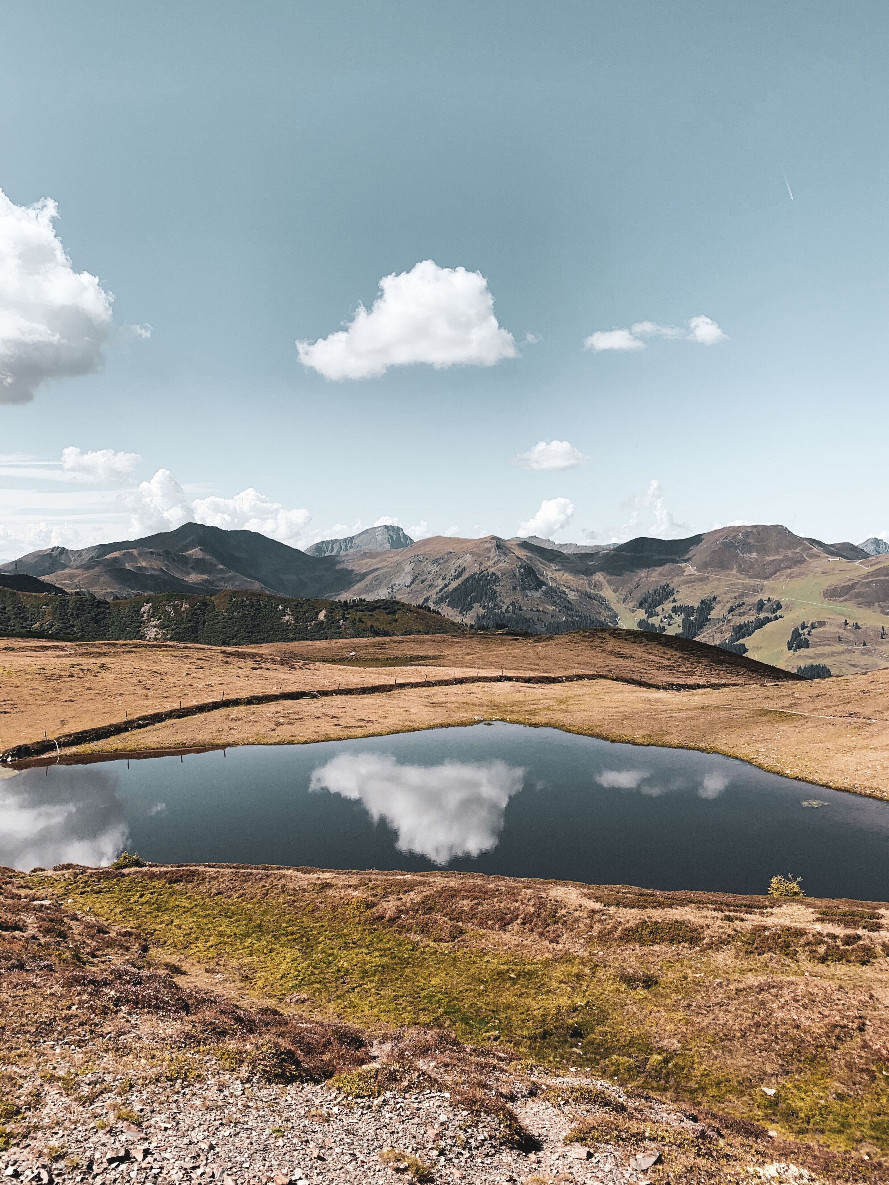 Paisaje montañoso con cielo despejado y un pequeño lago que refleja las nubes.