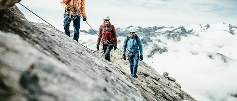 Three climbers ascending a rocky mountain path with a snowy mountain range in the background.