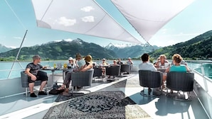 A group of people dining on a boat with a mountainous landscape in the background.