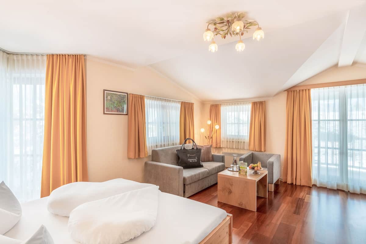 Ett hotellrum med en säng, en soffa, ett soffbord och ett skrivbord. Det finns gardiner vid fönstren och en kristallkrona hänger från taket.