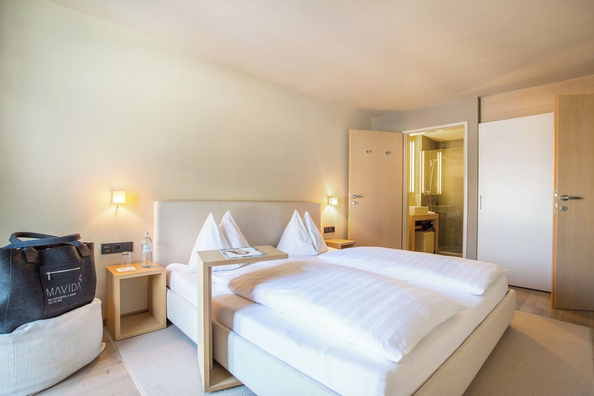 Ett hotellrum med en säng, sängbord, ett litet bord, en resväska och en garderob.