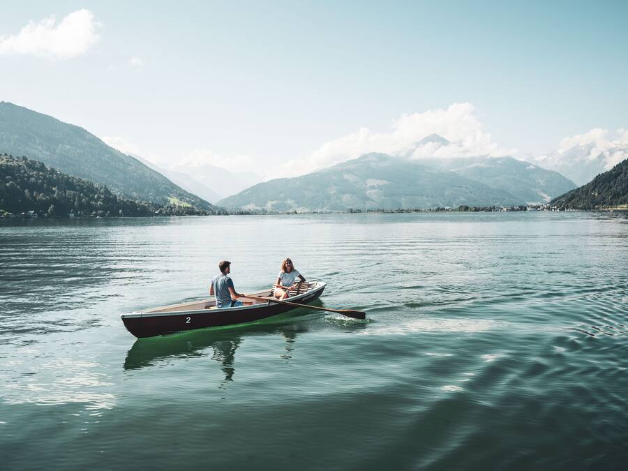 Un lac paisible où une barque à rames transporte deux personnes, le tout entouré de montagnes et sous un ciel dégagé.