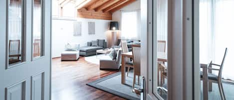 Een ruime woonkamer met een houten plafond, een bank, een eettafel met stoelen en een lamp.