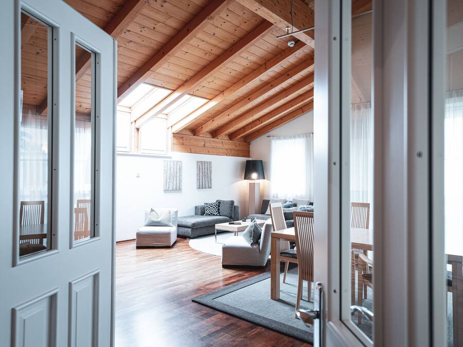 A spacious living area with a wooden ceiling, a sofa, a dining table with chairs, and a lamp.