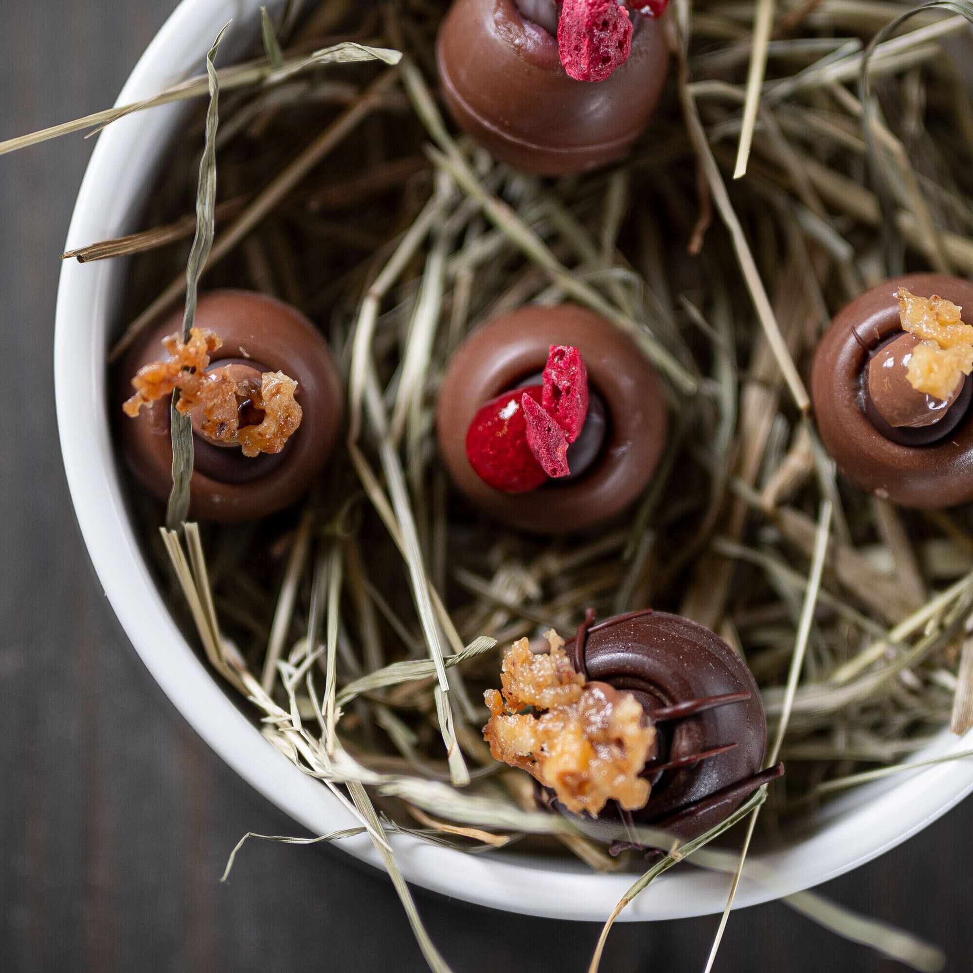 A bowl of chocolate-covered treats with a rustic straw background.