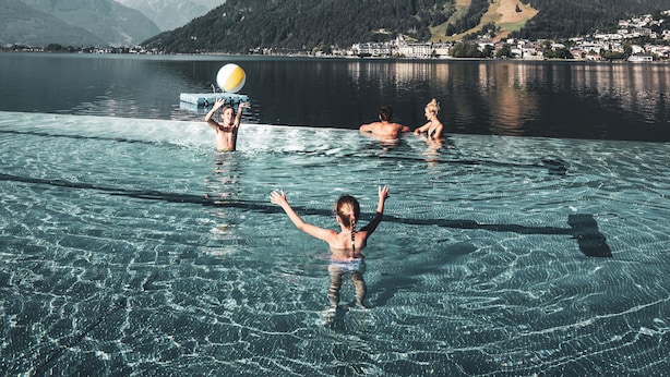 A clear view of a lake with mountains in the background, a boat, and people in the water.