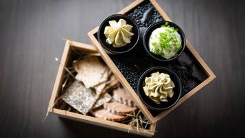 A wooden box containing various food items, including what appears to be cheese, crackers, and two bowls of dip.
