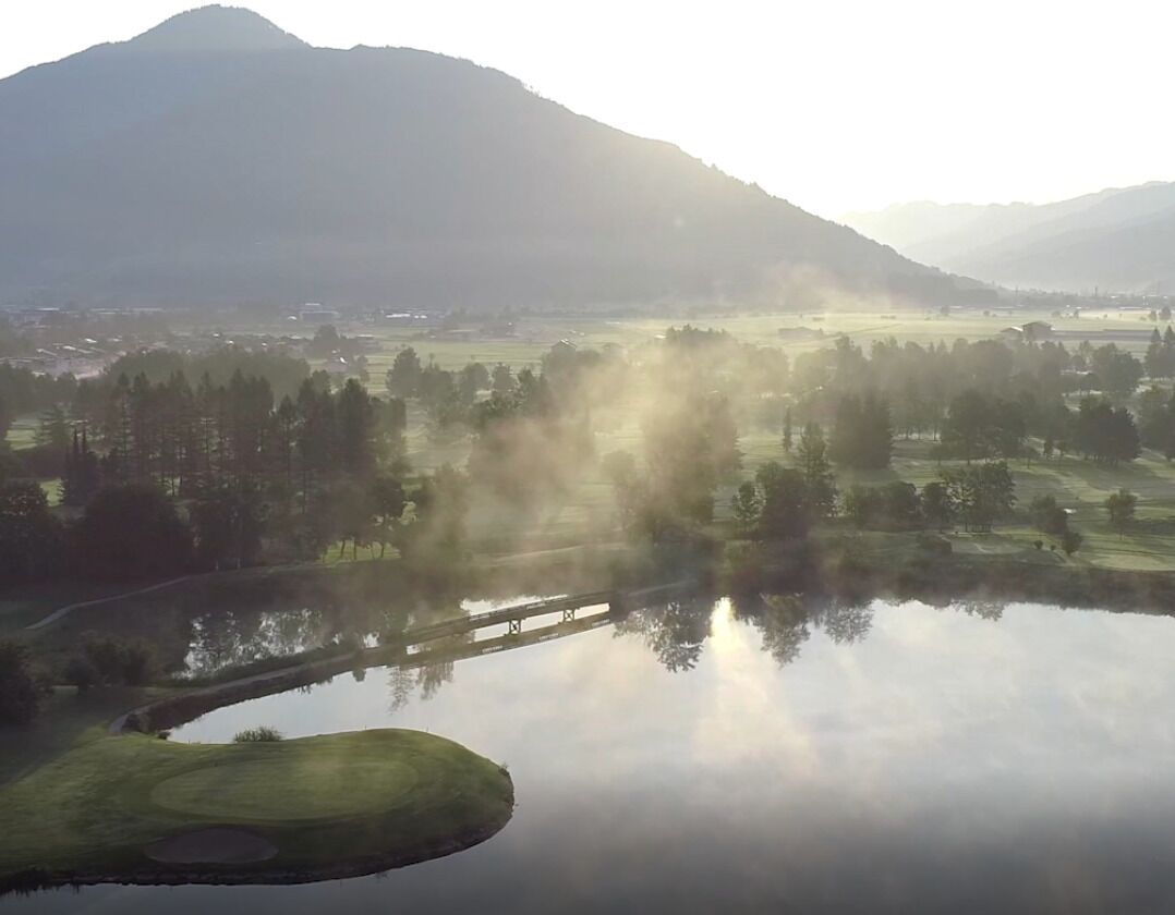 A serene landscape with a calm lake, a golf course, and a mountain in the background.