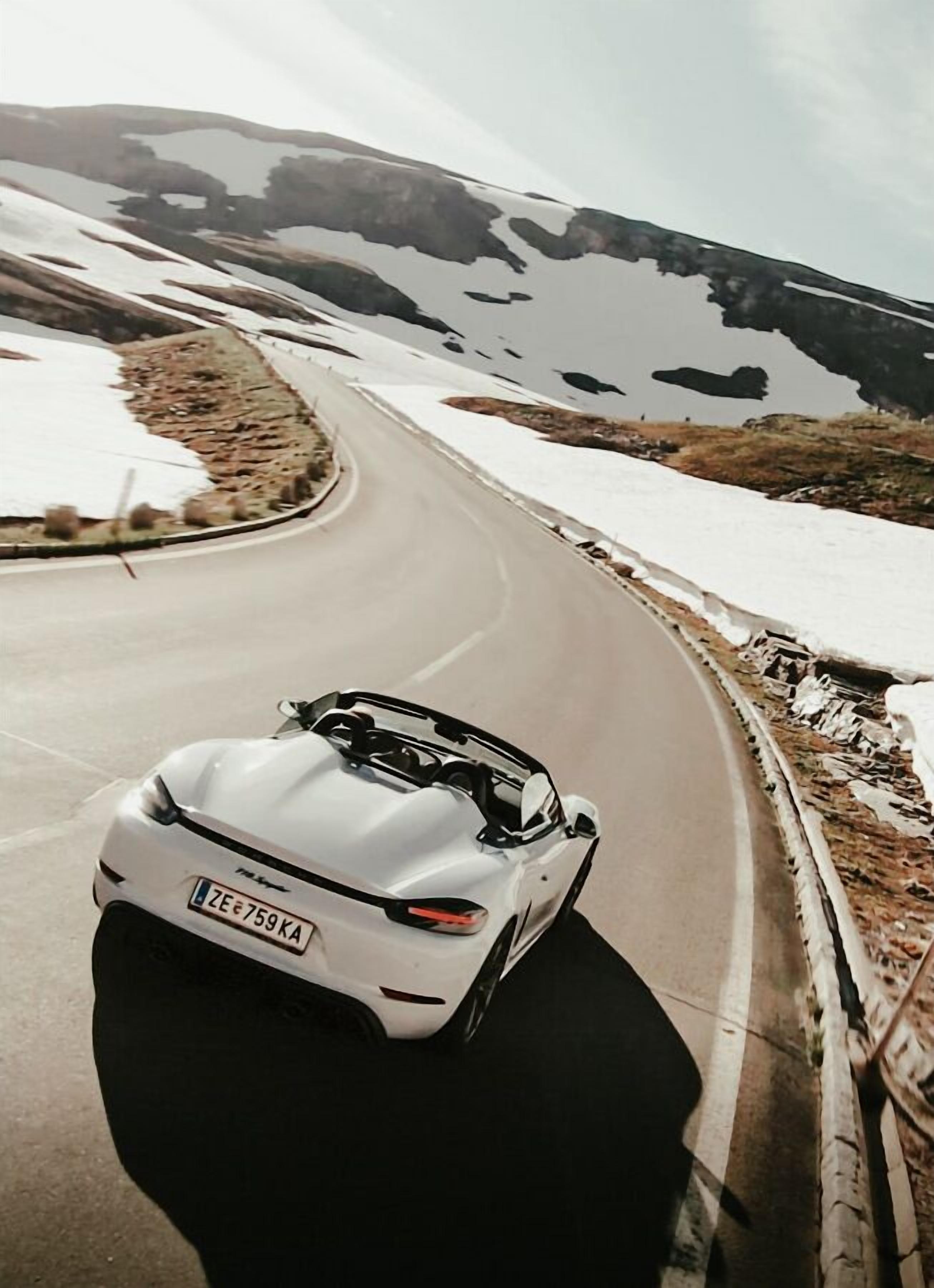 A white sports car driving on a winding road with snow patches on the sides.