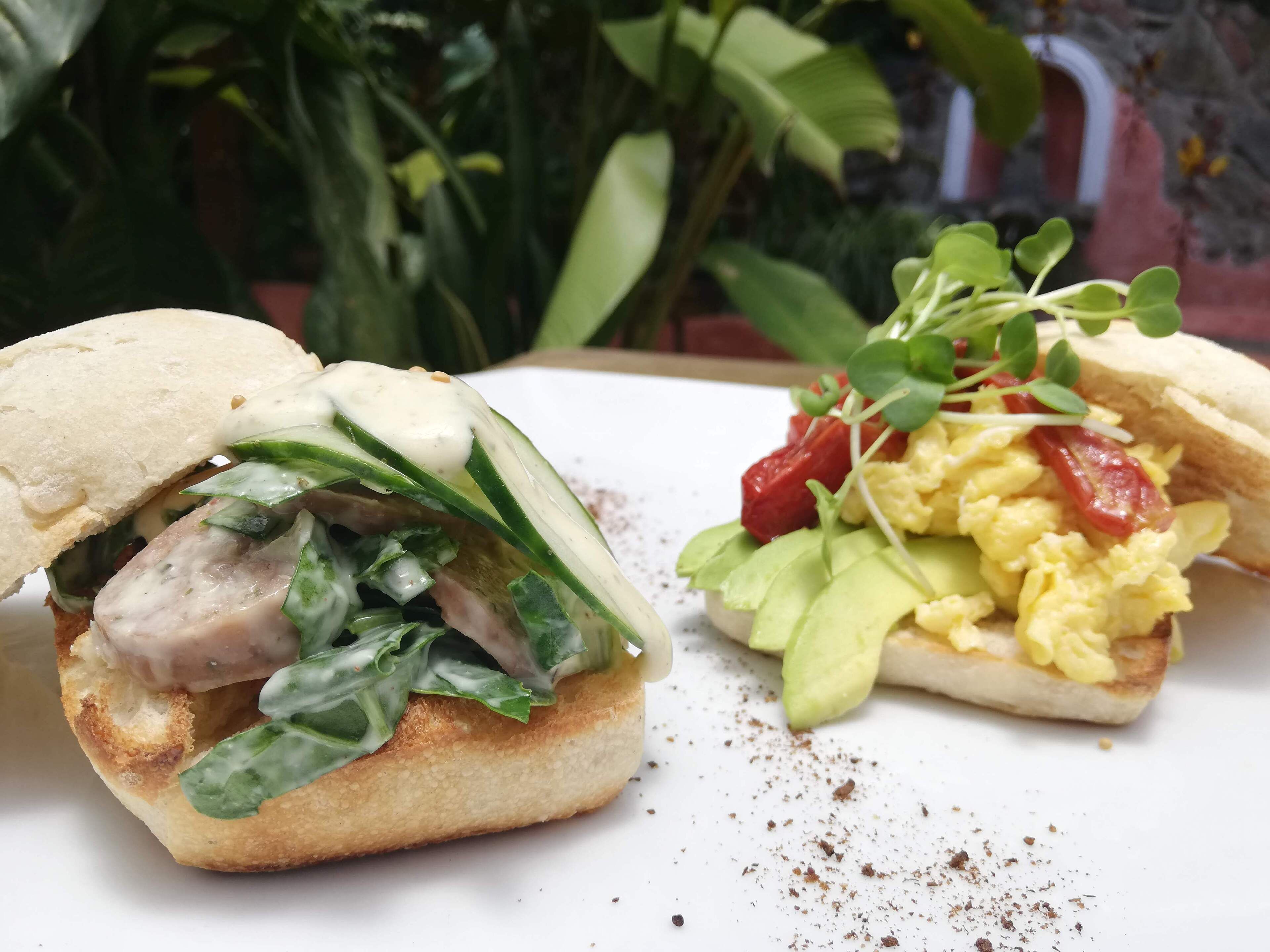 A sandwich with greens and a side of scrambled eggs with avocado and sprouts.