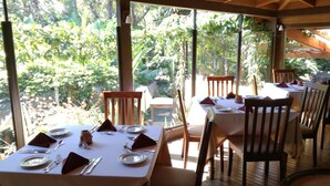Un restaurante con mesas dispuestas para comer, amplias ventanas que ofrecen vistas a zonas verdes y vigas de madera en el techo.