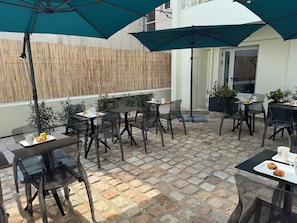 An outdoor patio with tables and chairs, umbrellas, and potted plants.