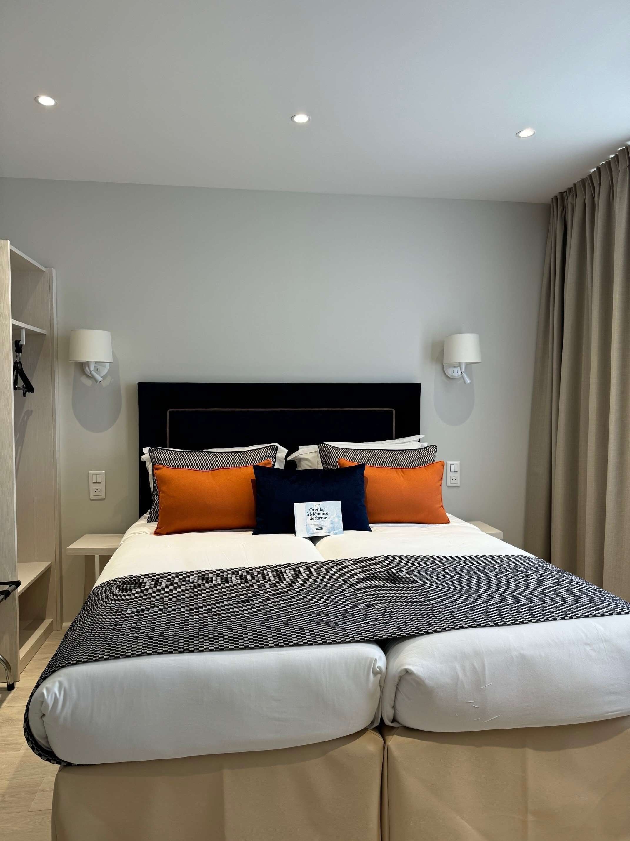 A hotel room with a large bed, two bedside tables, a wardrobe, and a ceiling light fixture.