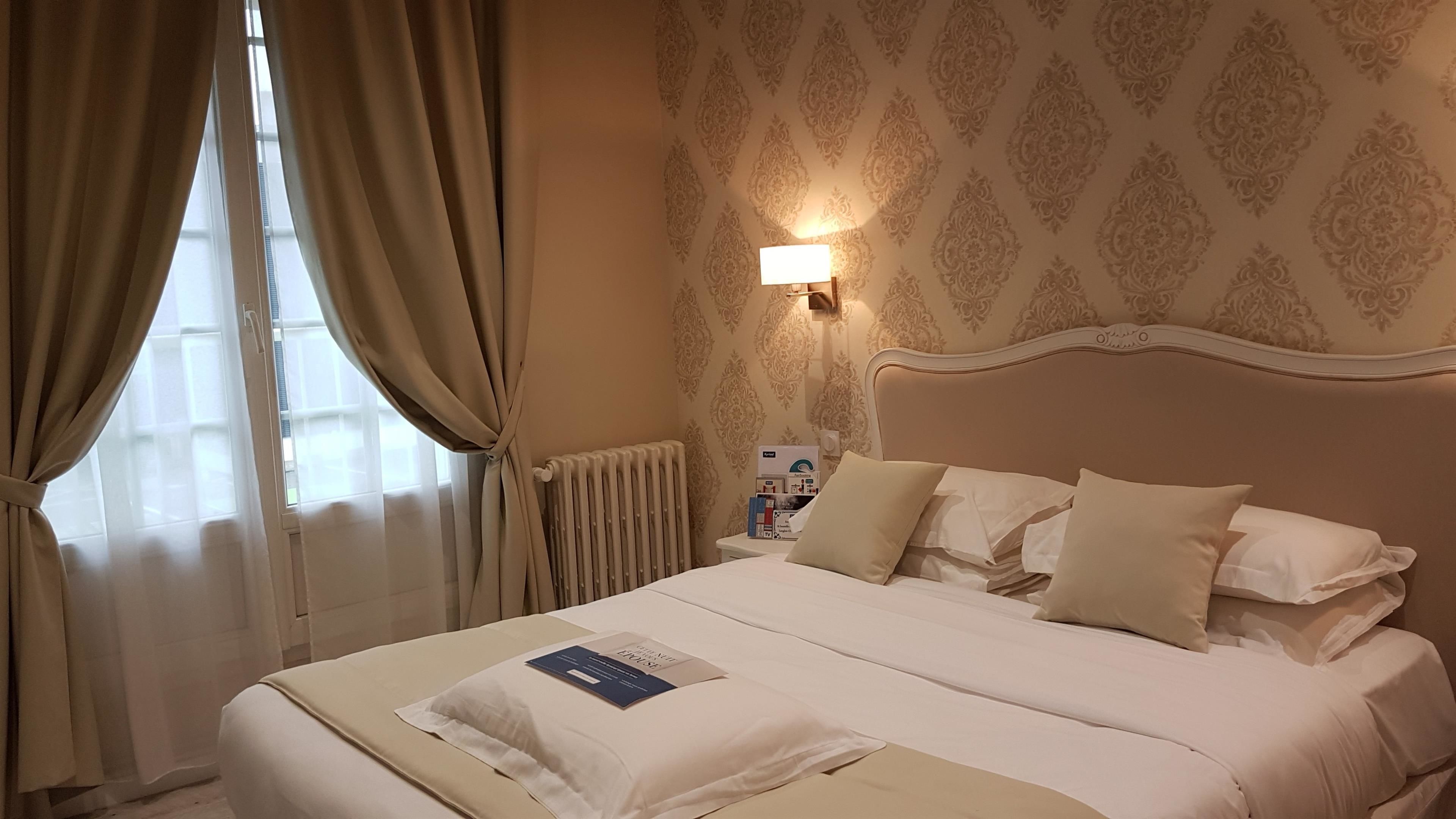 A hotel room with a neatly made bed, a bedside table with a lamp, and a radiator.