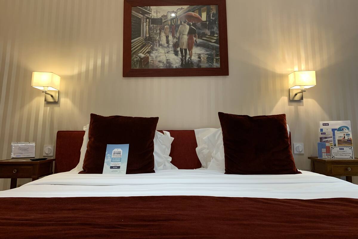 A hotel room with a large bed, two pillows, a framed painting on the wall, and two bedside lamps.